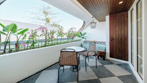 A balcony with a view of a garden, two wicker chairs, a round table, and a wooden ceiling. - Nuho Living (Pecatu)