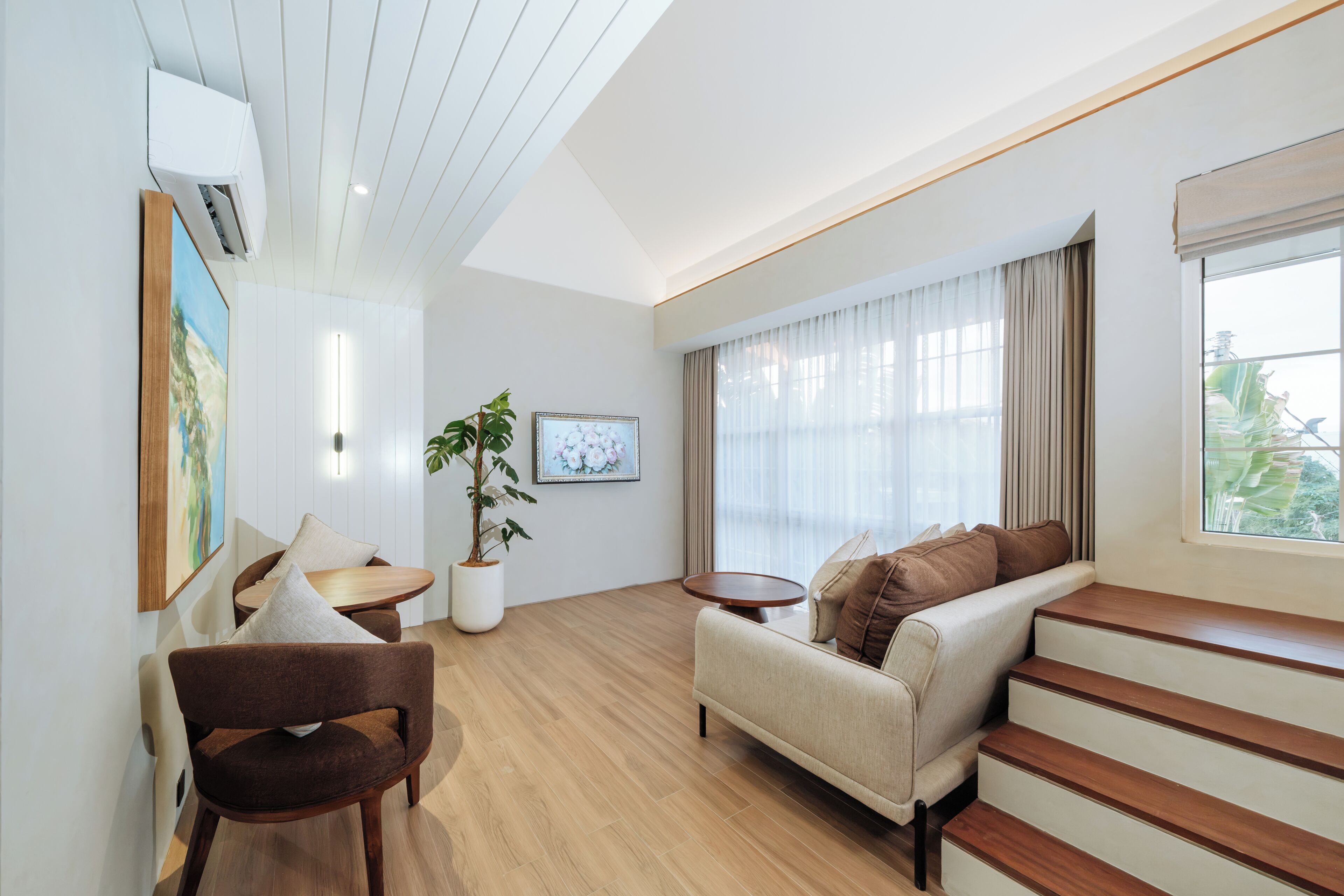 A modern living room with a sofa, armchair, and a small table. There is a potted plant and a painting on the wall.