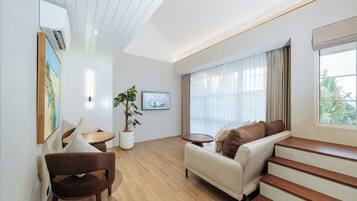 Una sala de estar moderna con sofá, sillón y una mesita. Se observa una planta en maceta y un cuadro en la pared.