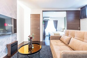 A modern hotel room with a sofa, a coffee table with a vase, a TV, and a door leading to a balcony. - FDS Luxe (OSAKA/NISHINARIKU/HANAZONOMINAMI)