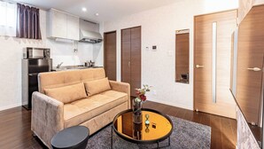 A modern living room with a sofa, a coffee table, and a kitchen area in the background. - FDS Luxe (OSAKA/NISHINARIKU/HANAZONOMINAMI)