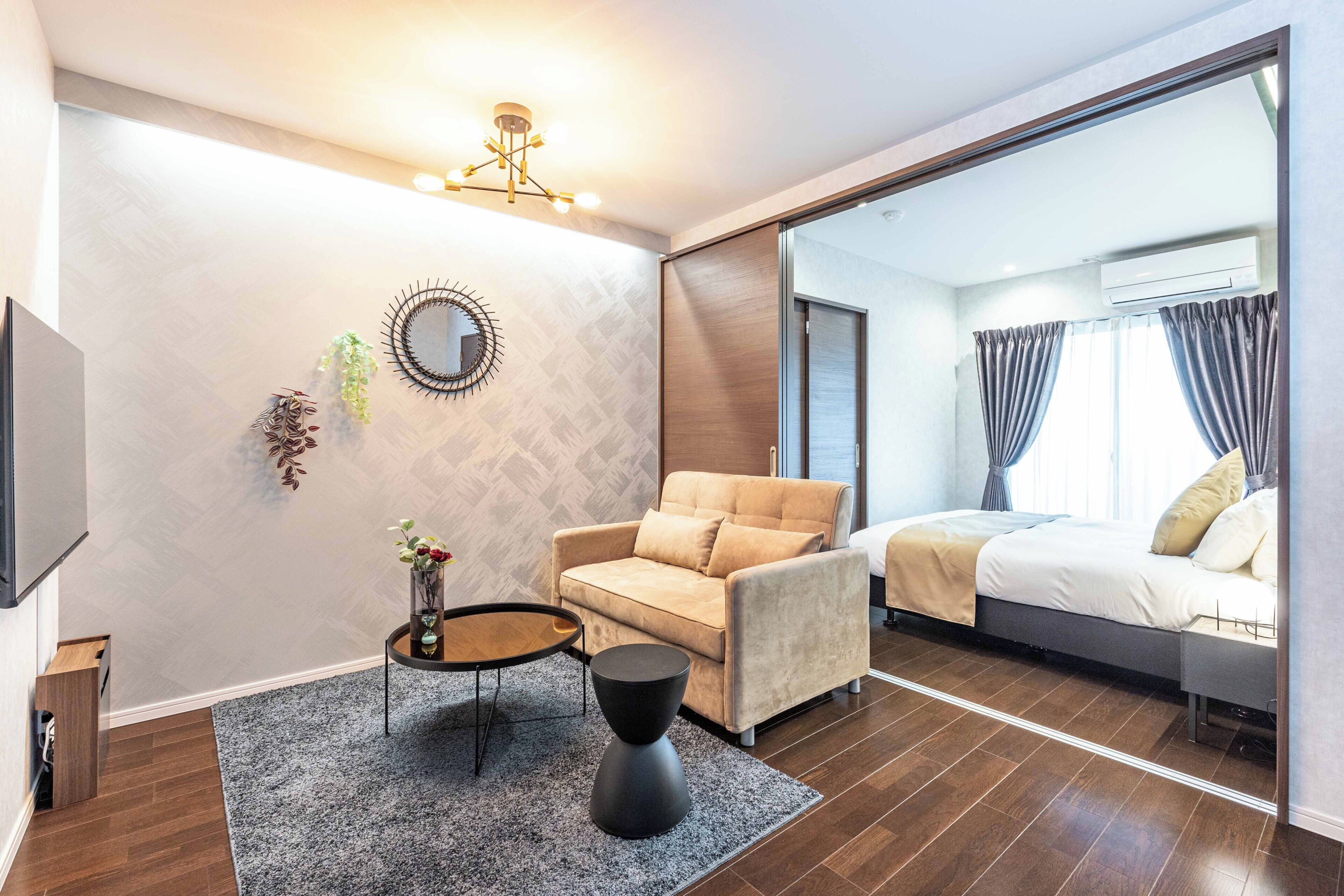 Ein modernes Hotelzimmer mit einer Couch, einem kleinen Beistelltisch, einem Spiegel und einem Bett mit Vorhängen.