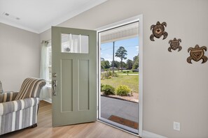 A room with a door leading to a view of a grassy area, a striped armchair, and three turtle wall decorations.