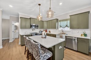 A modern kitchen with green cabinets, a central island, and pendant lighting.