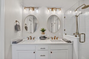 A modern bathroom with two sinks, a shower, and three wall-mounted lights.