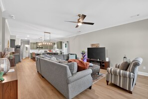 A modern living room with a grey sectional sofa, a striped armchair, a flat-screen TV, and a ceiling fan.