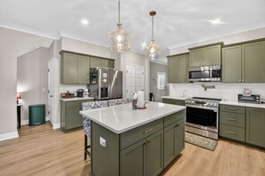 A kitchen with green cabinets, a central island, stainless steel appliances, and pendant lighting.