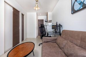 Ein modernes Wohnzimmer mit einem braunen Sofa, einem Holztisch, einem schwarzen Bürostuhl und einem Schreibtisch mit einem Computer.