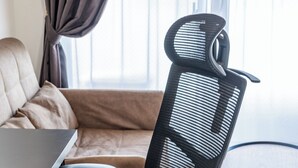 A black office chair with a mesh backrest and armrests, a five-point caster base, and a metal footrest. - FDS AIM (OSAKA/NISHINARIKU/TENGACHAYA)