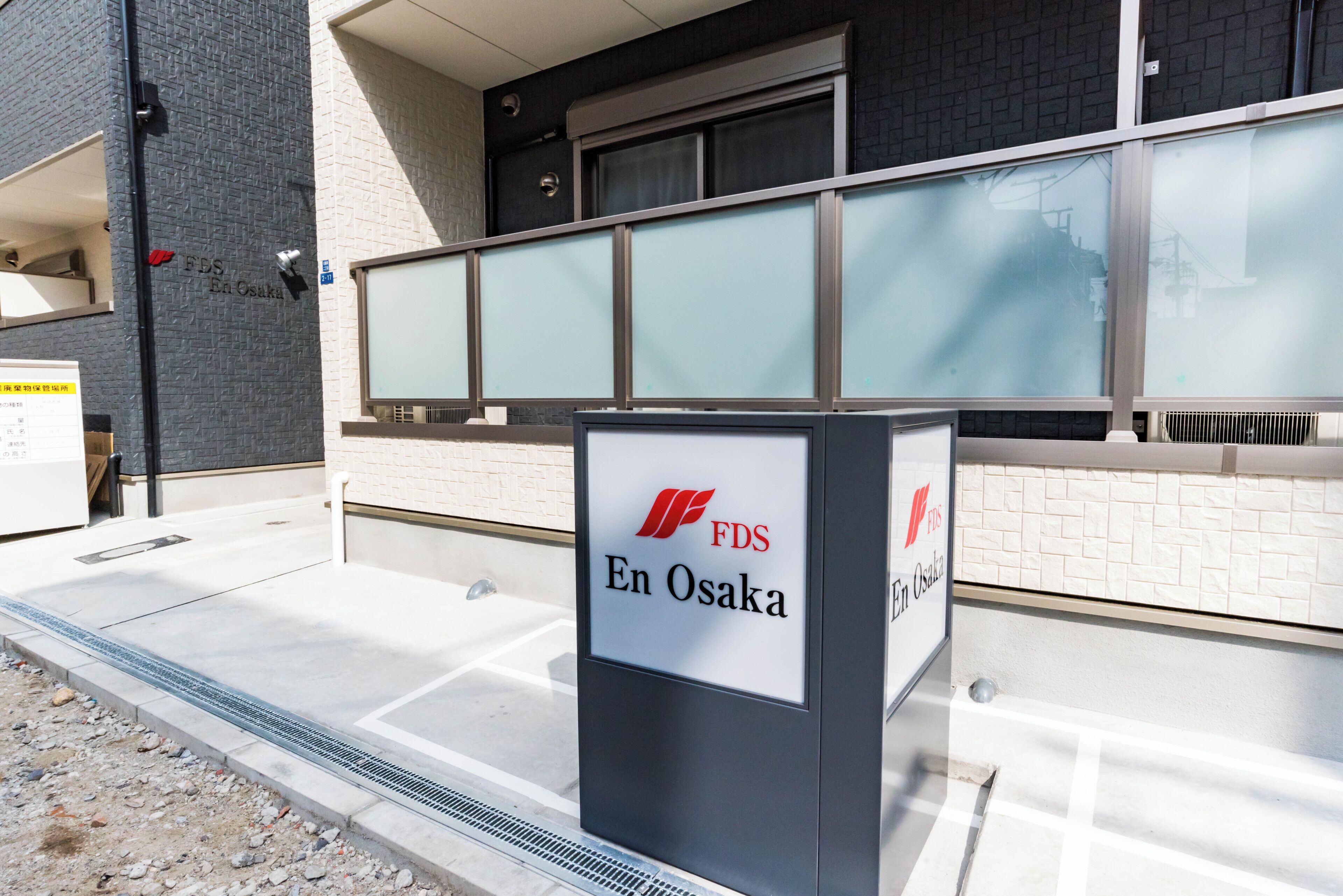 Un edificio con un cartel que dice 'FDS En Osaka' y un diseño moderno con fachada de baldosas y ventanas grandes.