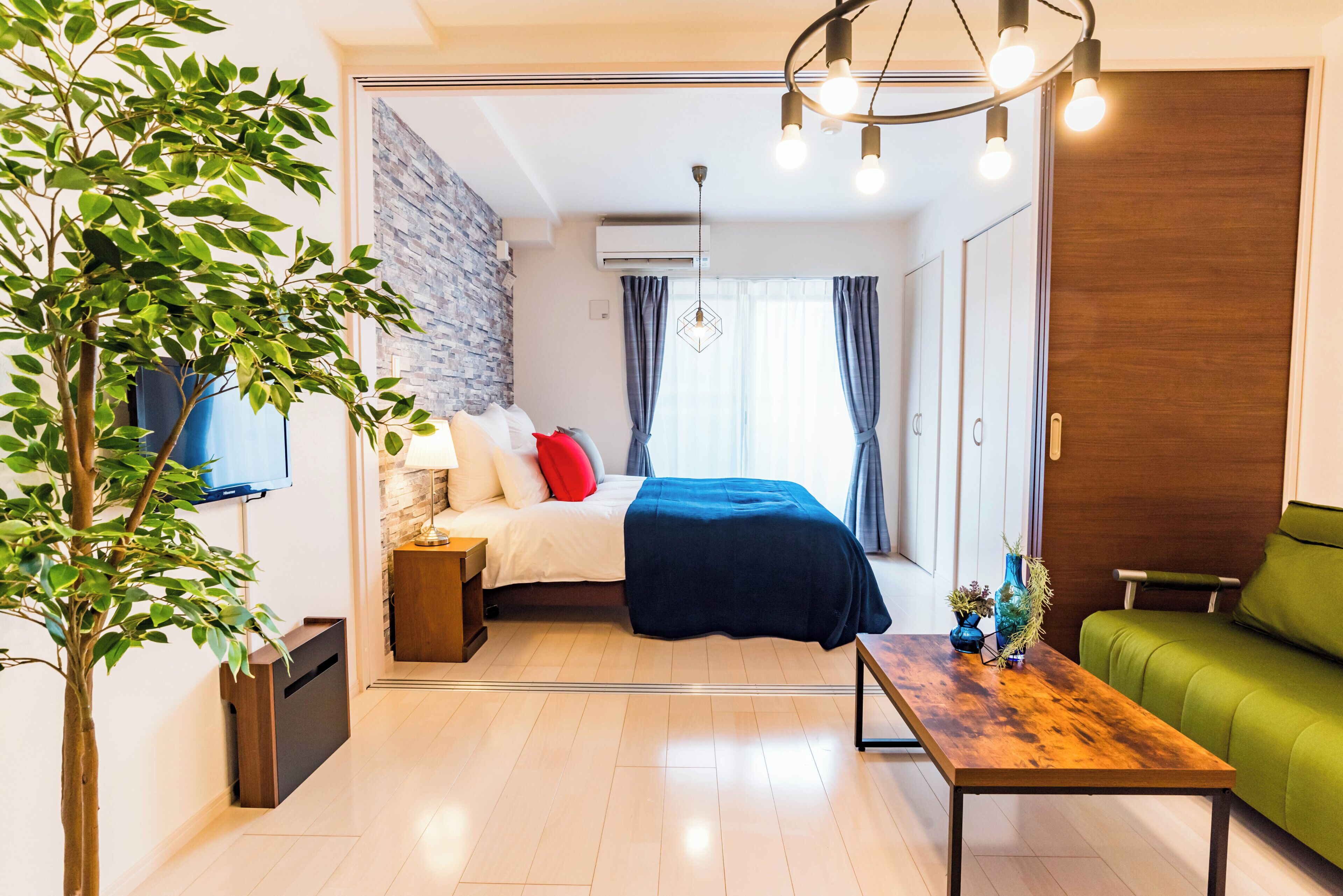 Una habitación moderna con una cama, un sofá verde, una mesa de centro de madera y una planta en maceta.