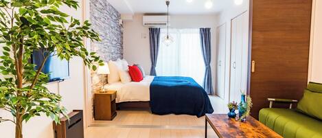 Una habitación moderna con una cama, un sofá verde, una mesa de centro de madera y una planta en maceta.