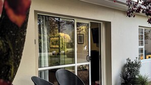 A modern building with a glass door entrance, a small patio with two chairs, and potted plants. - Peaceful Rural Retreat at the Base of Coronet Peak and linking to QT trails! (Speargrass Flat)