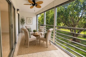 Ein Balkon mit Blick auf einen Garten, ein Deckenventilator und ein Tisch mit Stühlen.