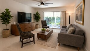 Ein Wohnzimmer mit Fernseher, zwei Sesseln, einer Couch, einem Couchtisch und einem Deckenventilator.