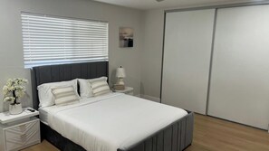 A bedroom with a bed, nightstands, a lamp, a potted plant, and a sliding door. - Chula Vista 5BR 3BA (Chula Vista)