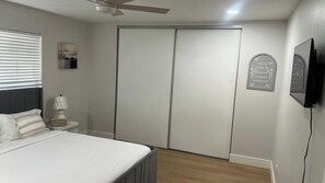 A bedroom with a bed, bedside table, lamp, ceiling fan, wardrobe, and wall-mounted TV. - Chula Vista 5BR 3BA (Chula Vista)