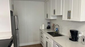 A kitchen with white cabinets, a refrigerator, a sink, a coffee maker, and a blender. - Chula Vista 5BR 3BA (Chula Vista)