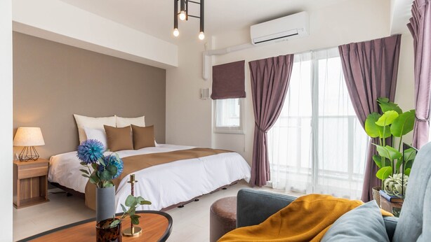A hotel room with a bed, bedside table, lamp, and a window with curtains.