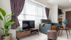A modern living room with a flat-screen TV, a sofa, a coffee table, and a potted plant.