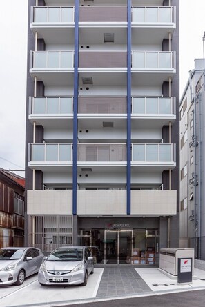 A multi-story building with a central blue stripe, a ground-level entrance, and parked cars.