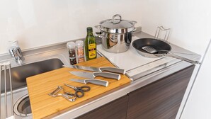 A kitchen with a sink, a cutting board, various knives, a frying pan, a pot, and a bottle of olive oil.