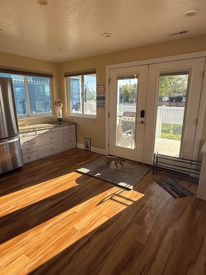 Una cocina con piso de madera, refrigerador, pileta, ventana con vista al patio trasero y puerta que da al exterior.