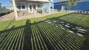 Een huis met een veranda, een kleine tuin en een blauw gebouw op de achtergrond.