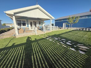 Une maison avec un porche, un petit jardin et un bâtiment bleu en arrière-plan.