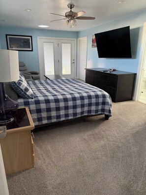 Une chambre à coucher avec un lit, un ventilateur de plafond, une télévision et une commode.