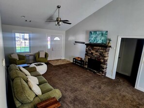 Una sala de estar con chimenea, ventilador de techo y televisor montado encima.