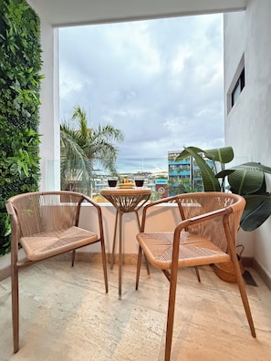 A balcony with wicker furniture, a glass table, and a view of buildings and palm trees. - Stylish & Luxurious Stay in the Heart of Playa del Carmen (Playa del Carmen)