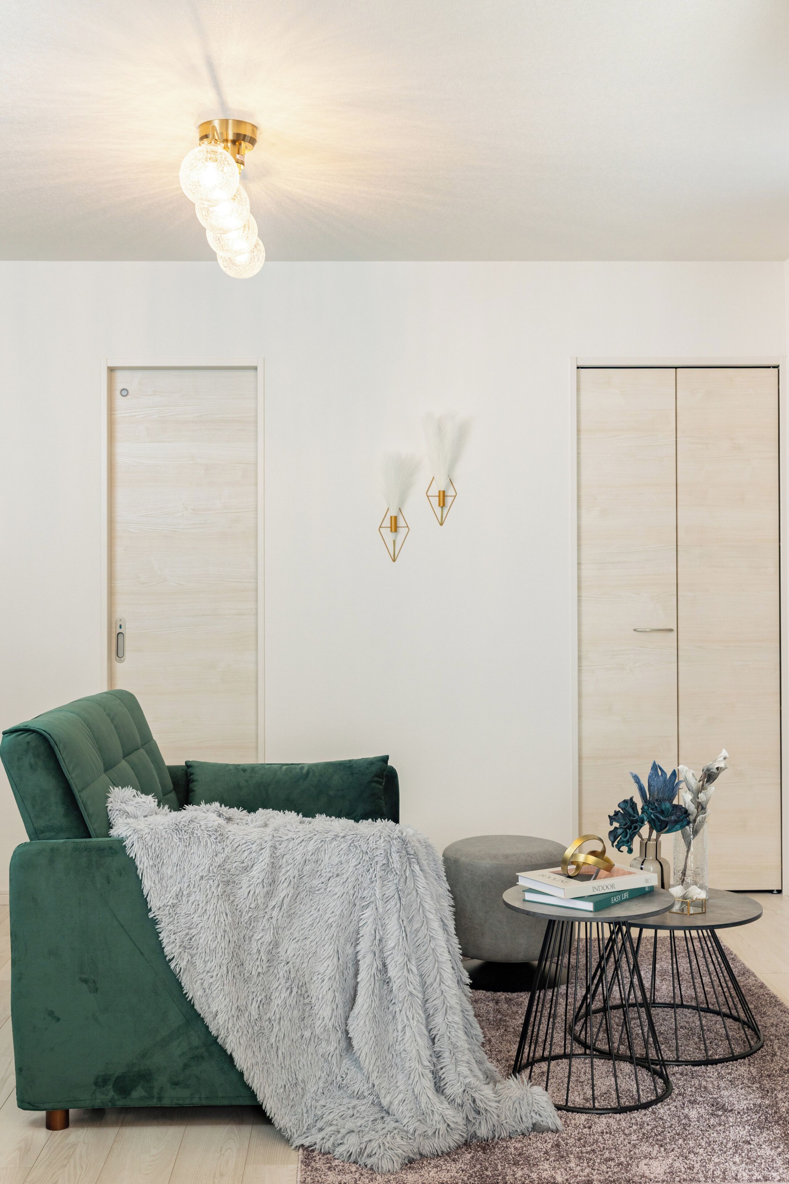 A modern living room with a green sofa, a grey furry throw, a round coffee table, and a ceiling light fixture.