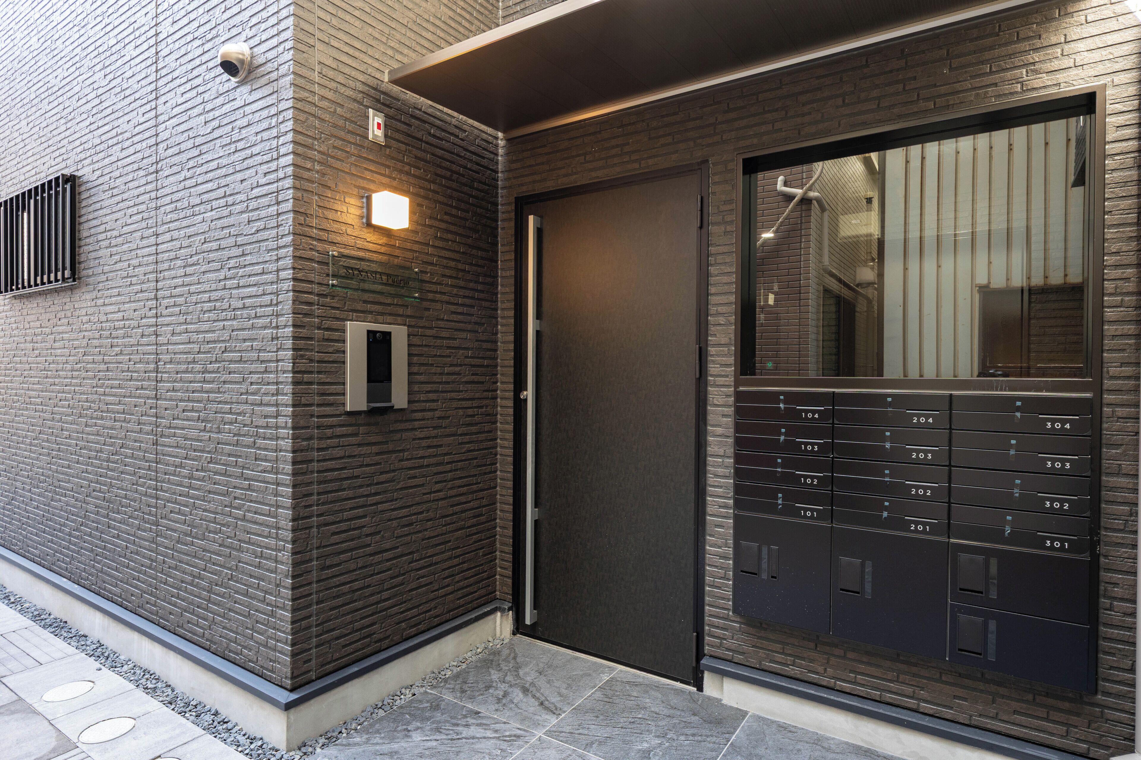 A modern building facade with a brick wall, a door, and a large mailbox with numbered mail slots.