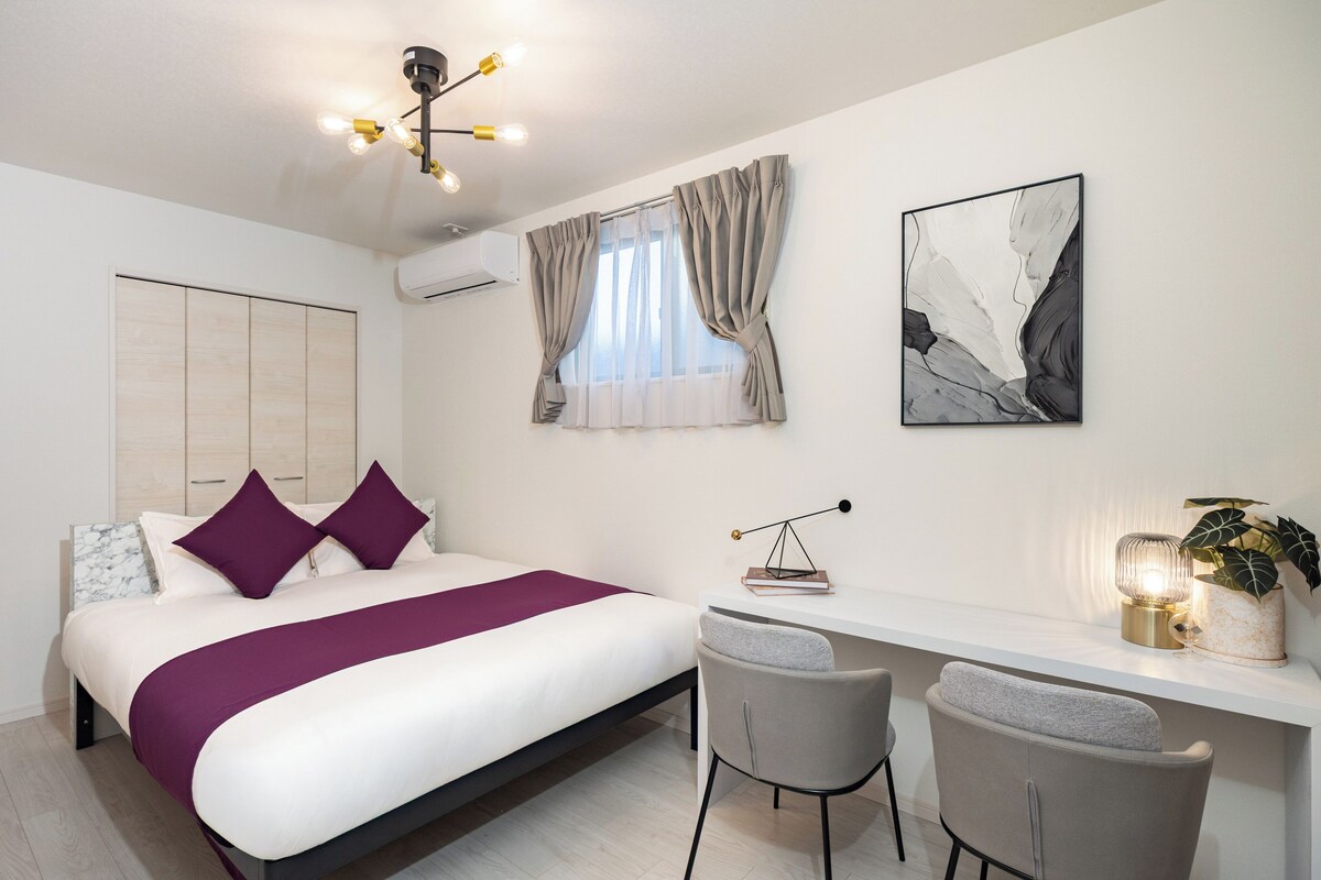 A modern bedroom with a bed, desk, chairs, and artwork.