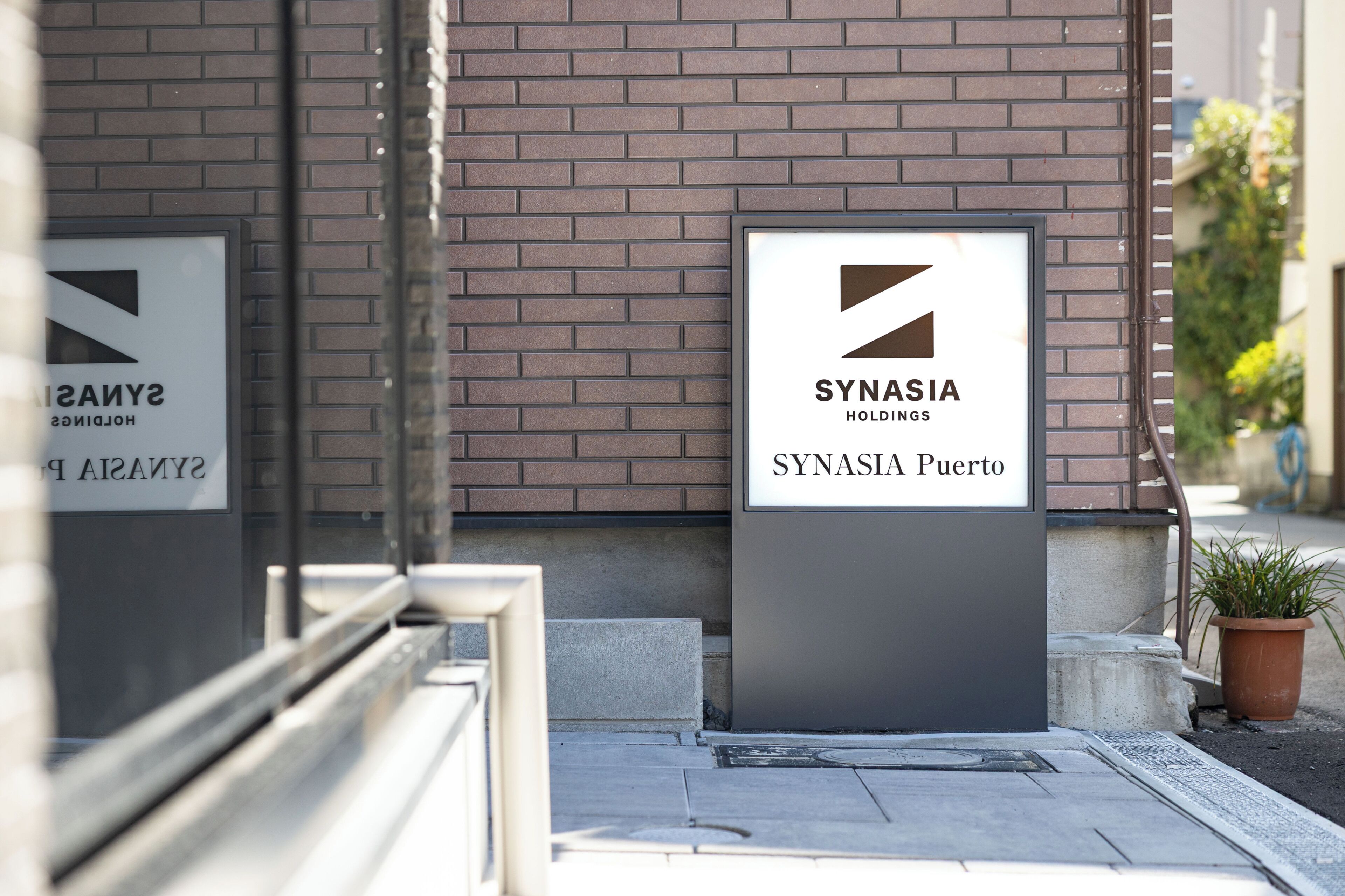 A sign for 'SYNASIA HOLDINGS' and 'SYNASIA Puerto' on a brick wall.