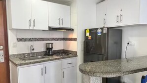 Eine Küche mit weißen Schränken, einem Gasherd, einer Kaffeemaschine, einem Kühlschrank und einer Arbeitsplatte aus Granit.