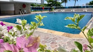 Ein Pool mit einer Steindekke, umgeben von tropischen Pflanzen und Palmen.