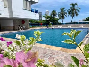 A swimming pool with a stone deck, surrounded by tropical plants and palm trees. - 17th Floor, Ocean View (Cartagena de Indias)