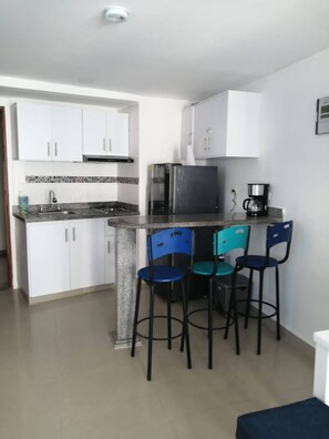 A compact kitchen with white cabinets, a stainless steel refrigerator, a coffee maker, and three bar stools. - 17th Floor, Ocean View (Cartagena de Indias)