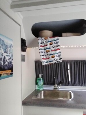 A kitchen with a sink, a bottle of hand soap, and a curtain. - Denali Scotty @ Creekside Campground (Willow)