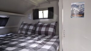 Ein Schlafzimmer mit karierter Bettdecke, einem Fenster mit Vorhängen, einem Poster an der Wand und einer Tür.