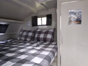 Un dormitori amb un llençol amb quadres, una finestra amb cortines, un cartell a la paret i una porta.