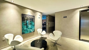 A modern waiting area with a large aquarium wall, white chairs, and a reception desk. - Edifício HIGH (Maceió)