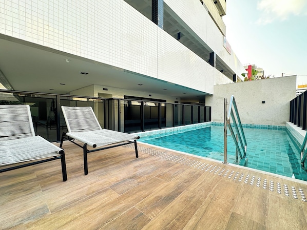 Ein Poolbereich mit zwei Liegestühlen, einer gefliesten Terrasse und einem Pool mit Glasabdeckung.