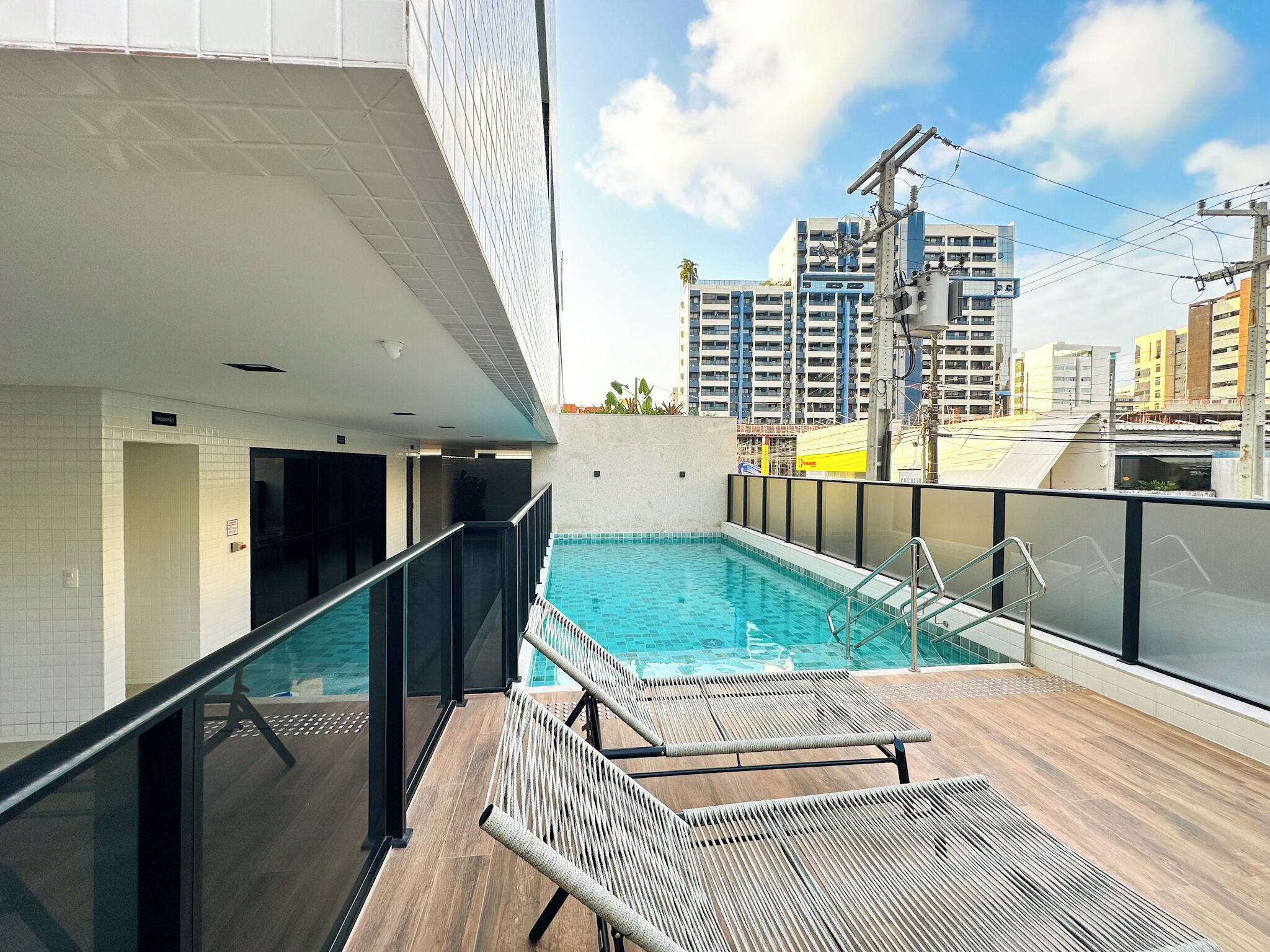 A rooftop pool with lounge chairs, a glass railing, and a view of surrounding buildings.