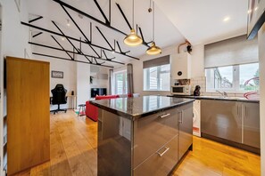 Una cocina moderna con electrodomésticos de acero inoxidable, piso de madera y un comedor con sofá rojo.