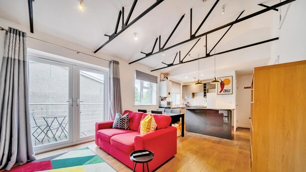 Eine moderne Wohnung mit einem roten Sofa, einem kleinen schwarzen Beistelltisch, einer Küchenzeile und einem Balkon mit Metallgeländer.