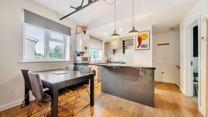 Eine moderne Küche mit Kochinsel, einem Essbereich mit Tisch und Stühlen sowie einem Blick ins Freie durch ein Fenster.