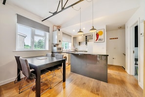 Una cocina moderna con una isla central, un comedor con mesa y sillas, y vistas al exterior a través de una ventana.